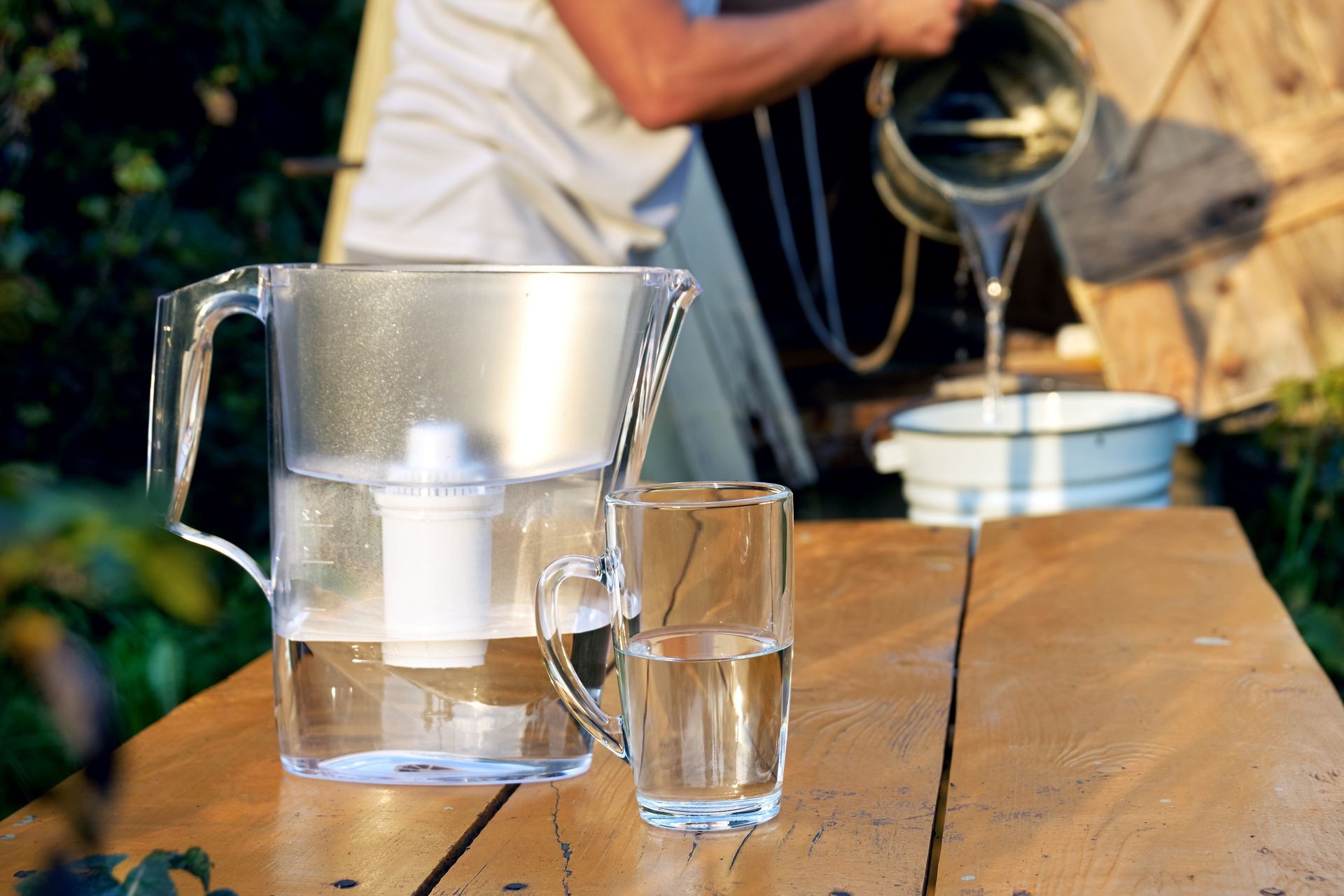 Filtration of a well water using a filter at countryside.  Water filter with a transparent cup with a man pouring water from a well on the blurred background                          